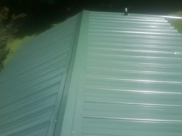 New green metal panels meeting at the ridge of a roof — Flat Roof Repair work by our crew in Gibson