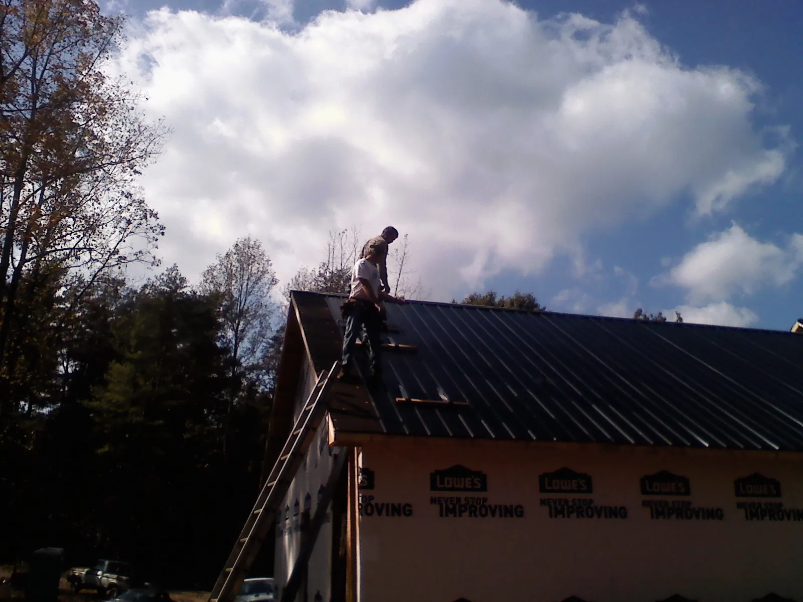 Roofer fastening dark metal panels high against a cloudy sky, from a Roof Inspection job in Gibson