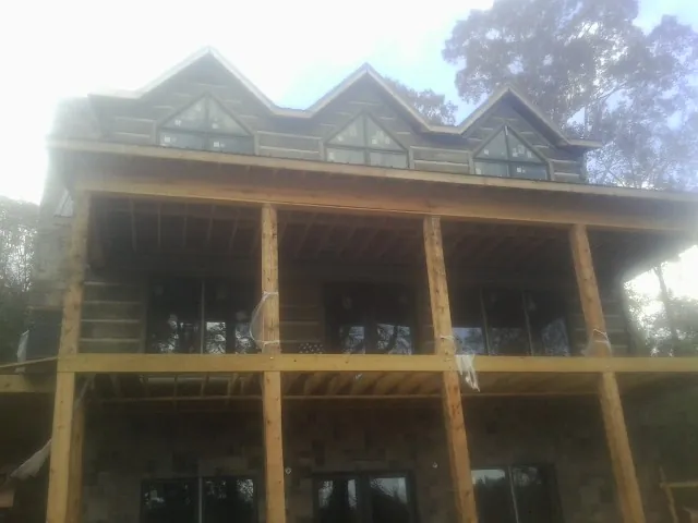 Dormers and porch framing on a large log home under construction — Roof Coating work by our crew in Gibson