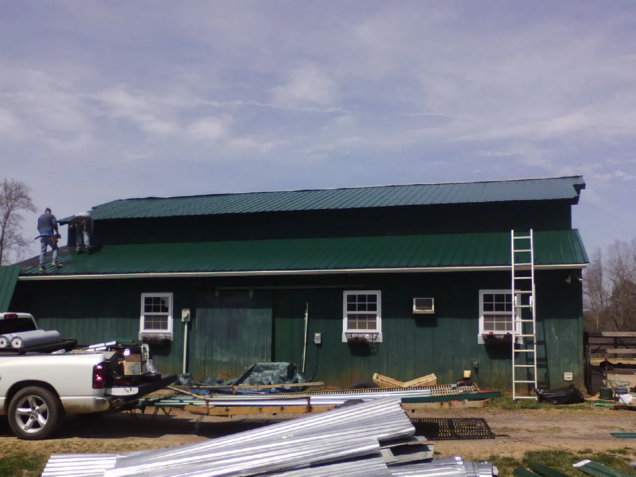 Crew installing green metal roofing on a large green barn in Gibson