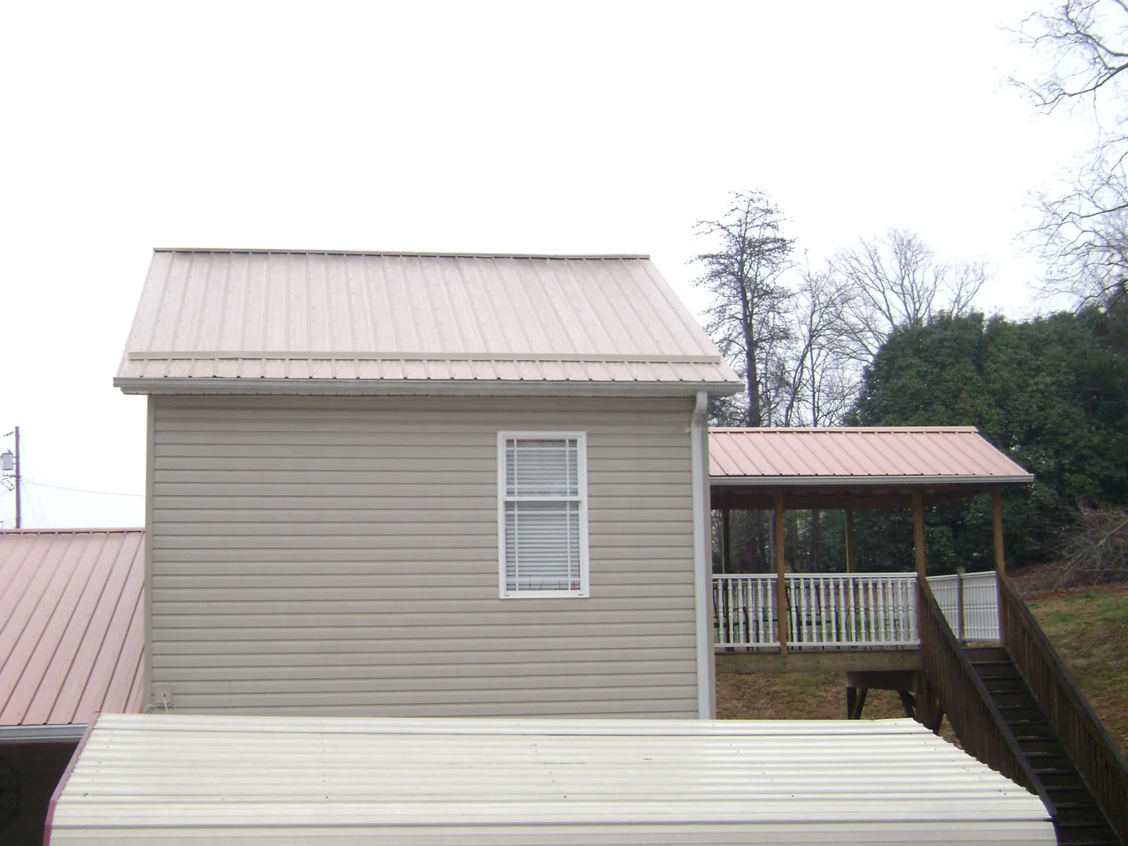 Tan metal roofs on a two story addition and attached porch, from a Roof Replacement job in Gibson